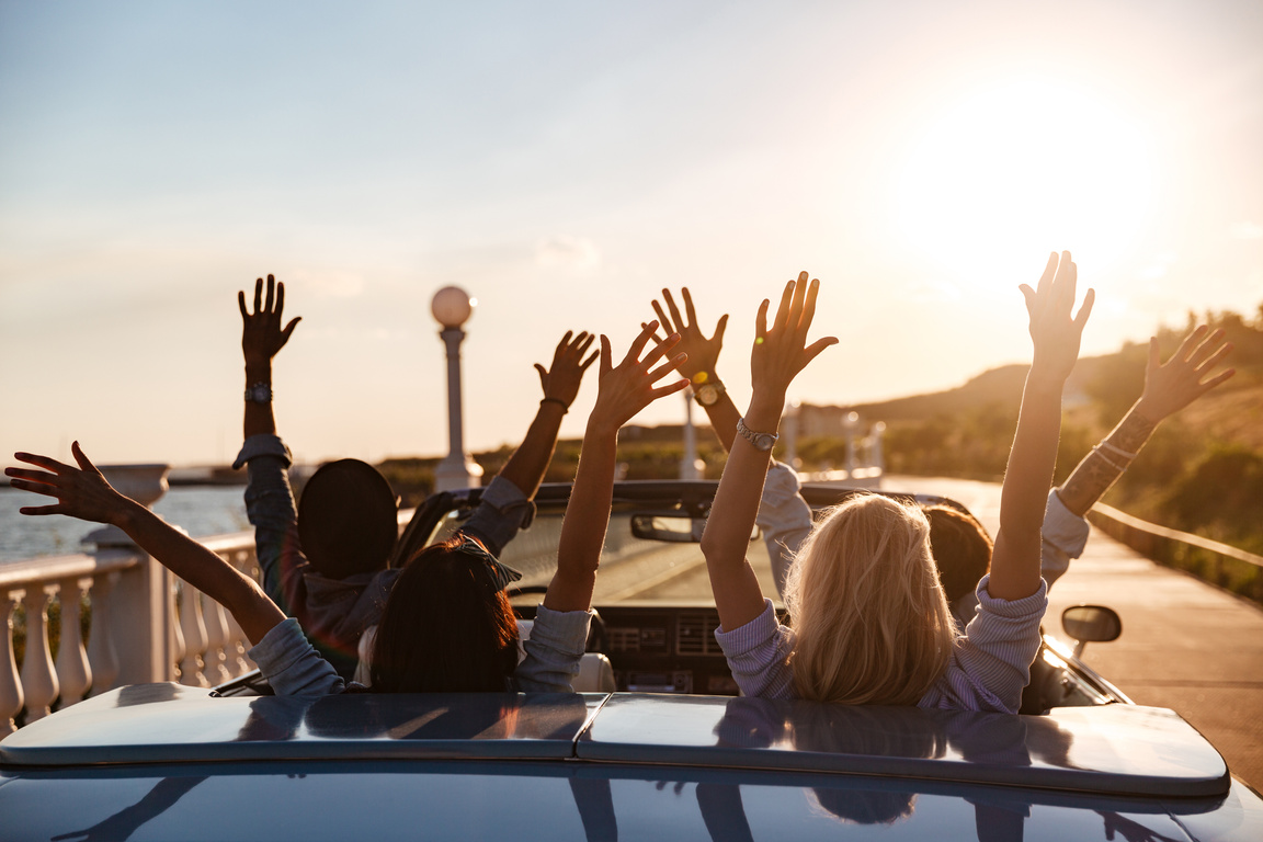 Back View of Happy Friends Driving Cabriolet with Raised Hands